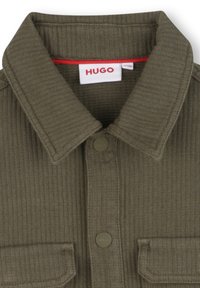 Olijfgroene corduroy overhemden met een button-down kraag, twee voorkruiden, en een kleine rode accent op het label. Gestructureerde stof.