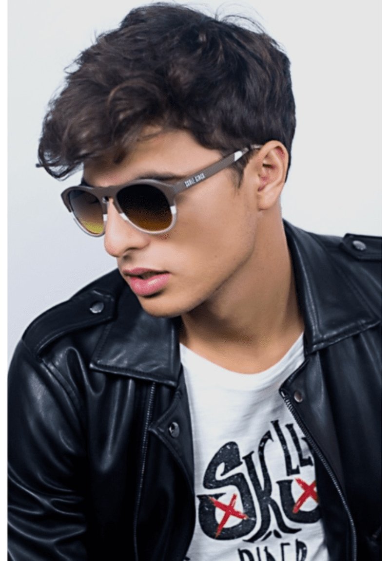 Gafas de sol con montura gris y lentes marrones degradados. Llevadas por una persona con chaqueta de cuero negra y camiseta gráfica blanca.