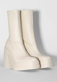 Kermanväriset nilkkurit sileällä nahkapinnalla, neliönmuotoiset varpaat ja paksut, korkeat alustakatteet. Minimalistinen muotoilu hienovaraisella ompelulla.