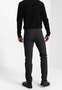Pantaloni grigi scuri su misura con una vestibilità strutturata, frontale piatto, texture sottile e tasche laterali, abbinati a un top nero a maniche lunghe.