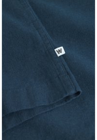 Material din bumbac de culoare bleumarin, cu margine pliată. Are o etichetă mică albă cu litere negre. Textură netedă, fără modele sau embellishments vizibile.