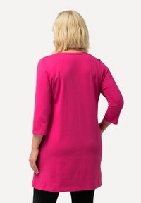 Langärmlige Tunika in leuchtendem Pink, aus weichem Stoff gefertigt. Sie hat einen runden Ausschnitt und fällt über die Hüften. Einfaches Design, ohne Muster.