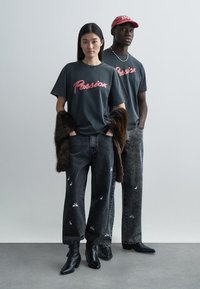 Tmavě šedá trička s červeným nápisem "Passion", spárovaná s černými džínami s bílými vzory králíka a černými kotníkovými botami.