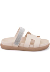 Sandales beige avec une semelle texturée, dotées d'une large sangle ornée de strass transparents et d'un design découpé. Style plat et à bout ouvert.