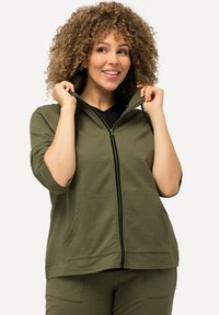 Sudadera con cremallera color verde oliva, con capucha, mangas cortas, bolsillos frontales y detalles de cremallera negra. Textura de tela suave.