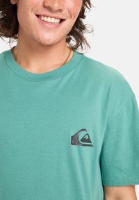 Mint green short-sleeve t-shirt made of soft fabric; features a small black logo on the left chest area; round neckline.