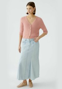 Rosa, kurzärmlige Strickjacke mit Knöpfen, kombiniert mit einem langen, hellblauen Jeansrock mit einem Schlitz an der Vorderseite und Nähten. Tragen mit beigen Schuhen.