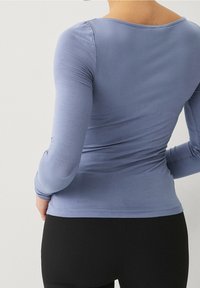 Pitkähihainen paita, joka on valmistettu pehmeästä, joustavasta kankaasta vaaleansinisena. Siinä on pyöreä kaula-aukko ja muotoilultaan kapea malli, joka myötäilee kehon muotoja.