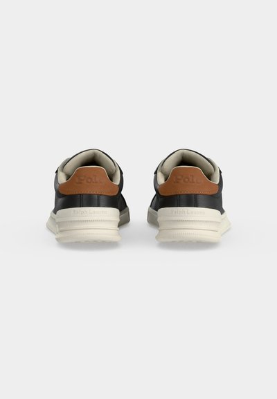 Ζευγάρι μαύρα sneakers χαμηλής κορυφής με λευκές σόλες και καφέ ταμπελάκια στην φτέρνα με ανάγλυφο "Polo,", σε απλό φόντο, από πίσω.