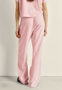 Ensemble de vêtements d'intérieur rose comprenant un pantalon large et un top court, fabriqué en tissu doux avec une texture lisse. Design simple sans motifs.