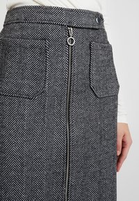 Jupe en mélange de laine à motif pied-de-poule noir et blanc, dotée d'une fermeture éclair à l'avant, de deux poches latérales et d'une taille haute.