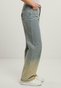 Jeans de mezclilla azul claro con un efecto degradado que va del azul al bronceado, corte de pierna ancha, dobladillo deshilachado y un bolsillo trasero con un detalle del logo oscuro.