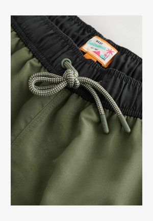 Shorts de bain vert olive avec une taille élastique noire, dotés d'un cordon de serrage avec des accents gris et d'une étiquette colorée portant l'inscription "NEXT Swimwear."