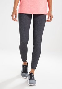 Leggings sportivi neri con una trama liscia, abbinati a sneakers grigie con chiusura a zip e dettagli in rete. Maglietta rosa brillante sopra.