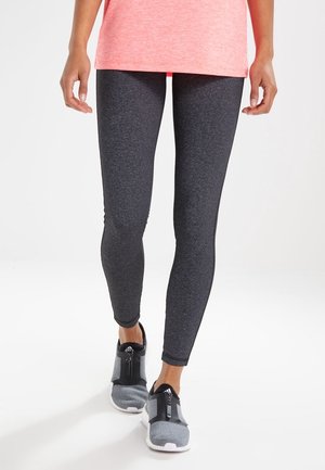 Leggings sportivi neri con una trama liscia, abbinati a sneakers grigie con chiusura a zip e dettagli in rete. Maglietta rosa brillante sopra.