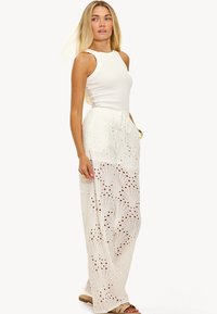 Witte mouwloze top gecombineerd met een vloeiende, kanten maxi rok met ingewikkelde uitsnijdingen en een elastische tailleband.