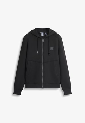 Sweat à zip noir avec capuche, poches avant, poignets côtelés et une patch logo texturé sur la poitrine. Fabriqué en tissu doux.