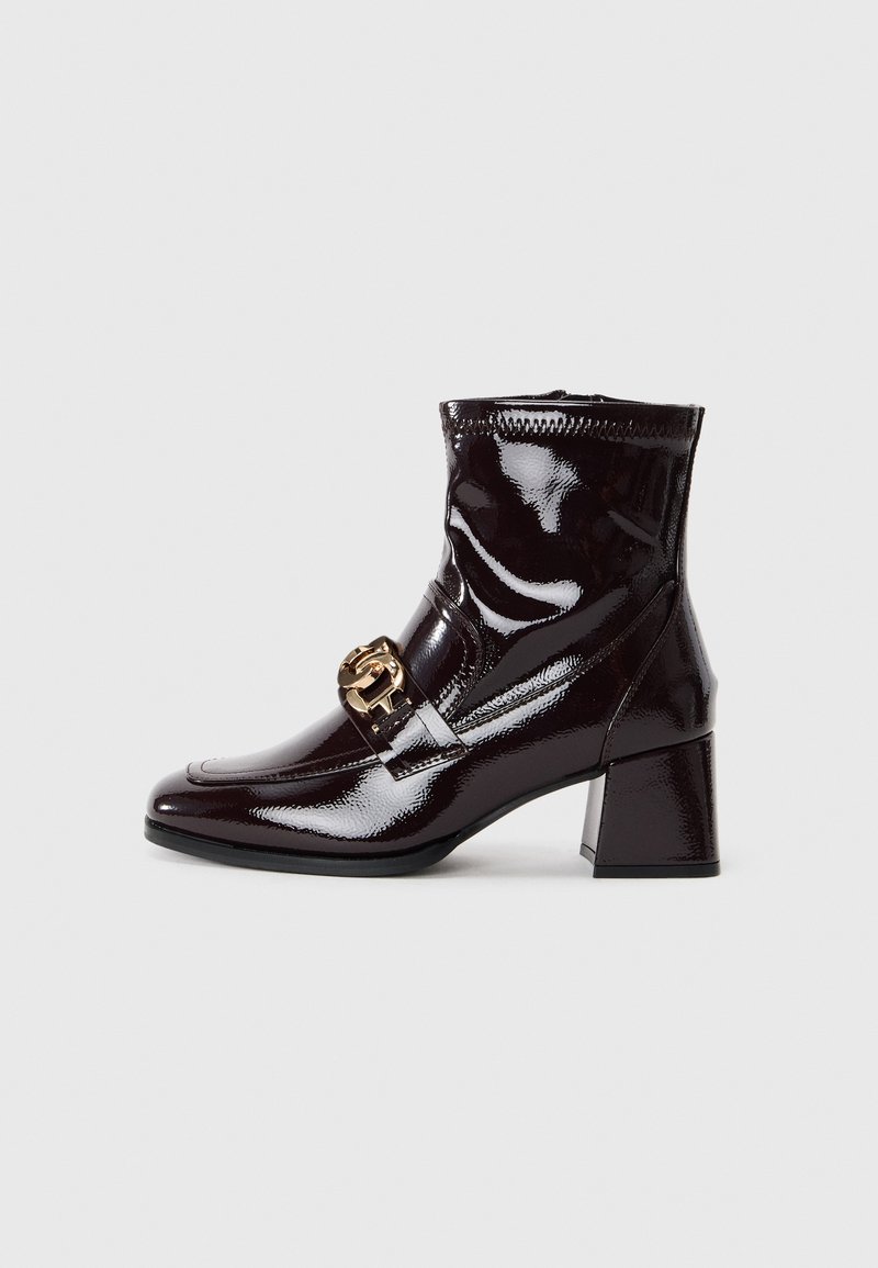 Botte cheville en cuir verni bordeaux foncé brillant avec talon bloc et boucle décorative dorée sur le côté.