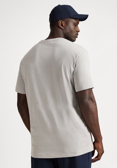 Γκρι βαμβακερό μπλουζάκι με κοντά μανίκια, άνετη εφαρμογή, λεία υφή και στρογγυλή λαιμόκοψη. Φορώντας ένα μπλε σκούφο. Θέα από πίσω.