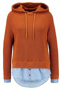 Oranssi neulottu hupullinen huppari, jossa on kiristysnyöri sekä resorit helmassa ja hihansuissa, päälle puettu vaaleansininen chambray-paita, jossa on kaartuva helma.