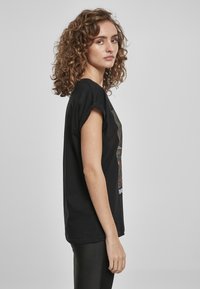 Schwarzes Baumwoll-T-Shirt mit Rundhalsausschnitt, aufgerollten kurzen Ärmeln und einem Grafikdruck auf der Vorderseite. Reguläre Passform mit geradem Saum.