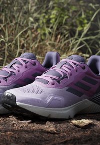 Lilla og sorte Adidas løbesko på en jordsti med græs i baggrunden.