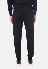 Pantaloni neri con una vestibilità su misura, dotati di due tasche posteriori e una trama liscia. L'orlo è leggermente affusolato, abbinati a scarpe nere.