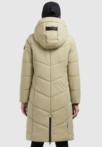 Beidzot puffer mētelis ar kapuci, kas izgatavots no bežā krāsā, ar chevron izšuvuma rakstu un pilnu garuma rāvējslēdzēju aizmugurē. Mīksts materiāls un brīvs piegriezums.