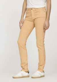 Jeans skinny orange clair en tissu mélangé coton, dotés d'une fermeture à bouton sur le devant et d'un design à cinq poches, assortis à des baskets blanches.