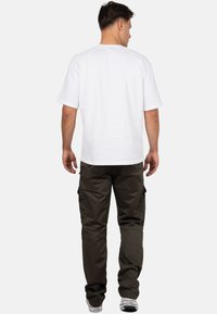 Weißes T-Shirt mit kurzen Ärmeln und Rundhalsausschnitt, kombiniert mit olivfarbenen Cargo-Hosen mit mehreren Taschen und einem lockeren Schnitt.