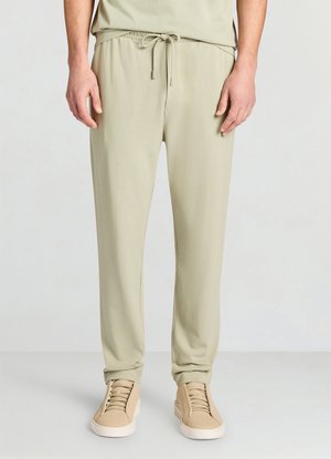 Pantaloni jogger verde chiaro con vita elasticizzata e coulisse regolabile, realizzati in materiale morbido, abbinati a scarpe da ginnastica beige.