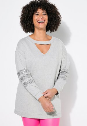 Sweatshirt gris avec un col échancré et un détail découpé. Les manches longues sont ornées de rayures en sequins argentés. Le tissu est doux avec une coupe décontractée.