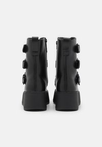 Bottes cheville en cuir noir à texture lisse, ornées de trois boucles de chaque côté et d'une semelle noire épaisse.