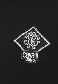 Czarny strój ozdobiony srebrnym, haftowanym logo w kształcie diamentu, przedstawiającym splecione litery i napis "cavalli UOMO" na dole.