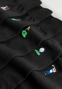 Calze nere con colorati ricami, tra cui un golfista, una luna, piante e un’altalena. Tessuto morbido e polsini a coste.