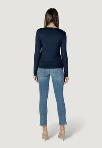 Maglietta a maniche lunghe blu navy con un design aderente, abbinata a jeans skinny azzurri. Presenta una texture liscia e dettagli di cucitura minimali.