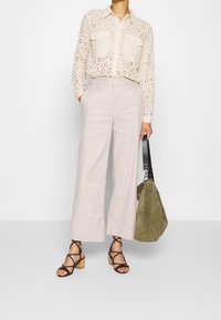 Krémová košile s výšivkou a dvěma náprsními kapsami, světle růžové kalhoty s širokými nohavicemi, hnědé sandály na podpatku se strappy pásky a zelená suková taška.