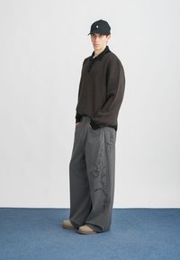 Μαύρο μίνι πουκάμισο με γιακά, γκρι στραπλωτές παντελόνες με μαύρες λουλουδάτες κεντήματα και μπεζ παντόφλες.