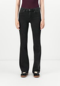 Svarte buksene med flared design laget av denim, med en tettsittende midje, to frontlommer og knappelukking. Sammen med svarte joggesko.