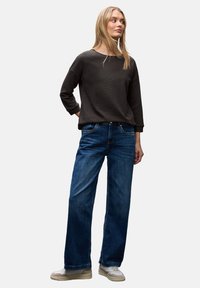 Mørkegrå ribbet langærmet bluse parret med blå vide denimbukser og lyse sneakers. Har en afslappet pasform og et enkelt design.