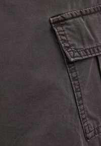 Grauer Stoff mit einer glatten Textur, versehen mit einer Taschenklappe oben. Die Nähte sind entlang der Kanten sichtbar und verleihen ein strukturiertes Aussehen.