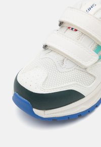 Valged sneaks roheliste aktsentidega, võrgust pealispind, kaks Velcro rihma, sinine välispind ja tekstuurilised detailid varvaste ja külgede peal.