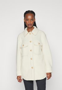 Witte fleece jack met een kraag, knoopsluiting en twee voorzakken. Voorzien van natuurlijke knopen en een relaxte pasvorm.