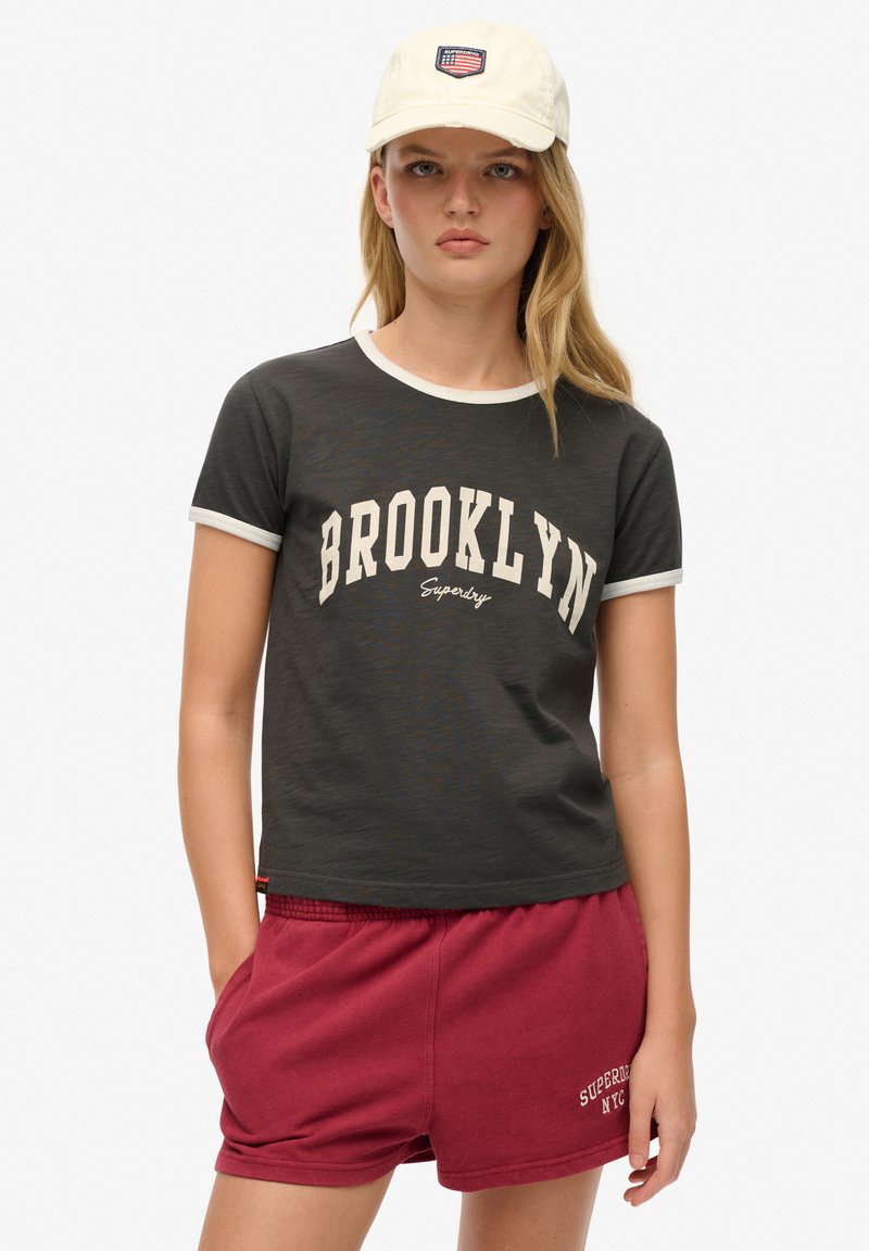Szara koszulka z krótkim rękawem z białym kołnierzykiem i grafiką "BROOKLYN"; zestawiona z bordowymi szortami z bocznymi kieszeniami i logo. Biała czapka z naszywką.