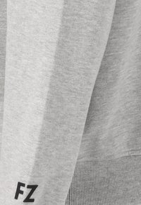 Närbild av ljusgrått tyg med ribbad fåll och svarta "FZ" initialer tryckta nära kanten.