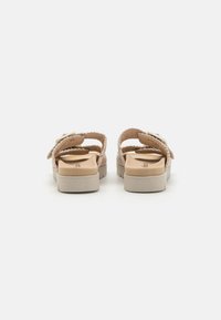 Beige sandaalit, joissa on punottu päällinen, säädettävä hihna ja tasainen pohjalevy. Karkeapintainen pohja ja brändäys sisäpohjassa.