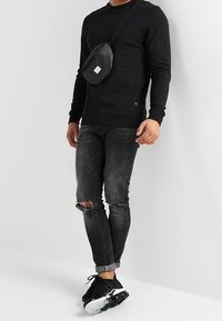 Felpa nera con scollatura rotonda, abbinata a jeans neri strappati e sneaker nere. L'accessorio include una piccola borsa a tracolla nera.