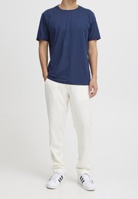 Marineblauwe T-shirt met korte mouwen, gecombineerd met witte linnen broek en witte sneakers met zwarte strepen. Eenvoudig, casual ontwerp en comfortabele pasvorm.