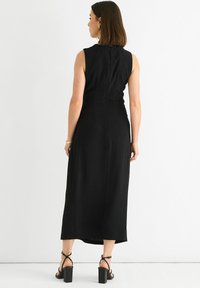 Black, sleeveless midi dress with a fitted silhouette, back zipper, and smooth texture. Worn with black block-heeled sandals.