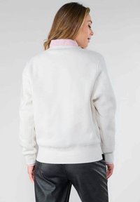 Sudadera blanca con cuello redondo y mangas largas, que presenta una tela texturizada y un interior del cuello de rayas rosas. Vista trasera.